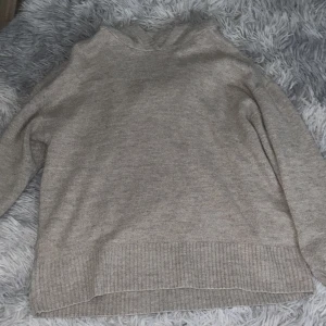 Beige stickad hoodie från Lindex - Mysig beige stickad hoodie från Lindex med ribbade muddar och nederkant. Perfekt för kyliga dagar och har en avslappnad passform med huva. Passar dig som gillar enkel och stilren design. Passar även 164-168.