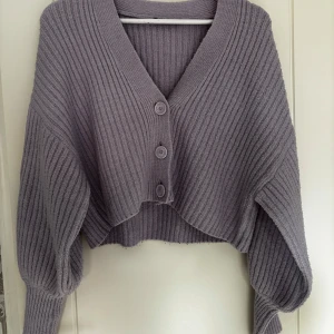 Ljuslila croppad kofta från Gina Tricot - Superfin ljuslila kofta från Gina Tricot. Tröjan är stickad med ribbad struktur, har croppad passform och stora ärmar. Stängs med tre knappar framtill och har en djup v-ringning. Perfekt för lager-på-lager-stil.