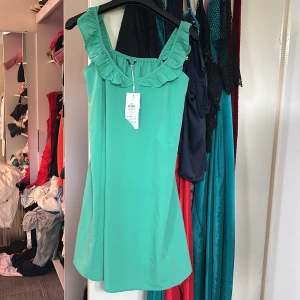 Turkos klänning med volang - Säljer en söt turkos klänning med breda axelband och volangdetalj längs urringningen. Klänningen har en rak passform och är perfekt för sommarens alla tillfällen. Superskön och lätt att bära.