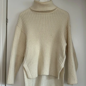 Beige ribbstickad polotröja - Säljer en beige ribbstickad polotröja med lång ärm och hög krage. Tröjan har slitsar på sidorna vilket ger en avslappnad look. Använd fåtal gånger.