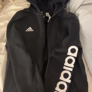 Svart zip hoodie från Adidas - Orginal pris: 350! FIN hoodiejacka från Adidas med dragkedja och stor vit Adidas-logga på ena ärmen samt mindre logga på bröstet. Tröjan har huva och är långärmad och har en lev insida vilket gör den väldigt varm och mysig!❤️