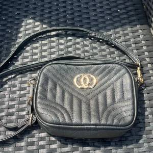 Väska - Snygg svart axelväska. Väskan har justerbar axelrem. Kommer tyvärr inte till användning. Mått: 20 cm lång, 15 cm hög. 