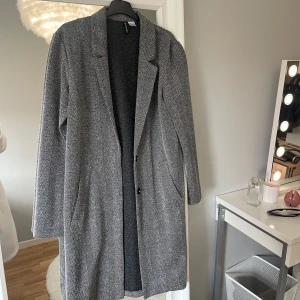 Grå kappa från H&M Divided - Säljer en lång, grå kappa från H&M Divided i storlek XS. Kappan har ett väldigt tunt material och passar därför super till sena sommarkvällar. Perfekt för dig som gillar stilrena och tidlösa plagg 😊
