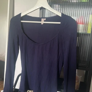 Mörkblå långärmad topp urringad med spets detaljer fram  - Säljer en enkel och stilren mörkblå långärmad topp med rundad halsringning och diskret spetskant. Perfekt att matcha med jeans eller kjol för en clean look. Supermjuk och skön mot huden!