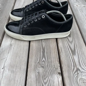 Svarta sneakers med vit sula - Säljer ett par svarta sneakers med vit sula. Skorna har snörning och en snygg kombination av mocka och glansigt material på tån. Perfekta för en stilren vardagslook.