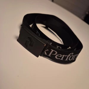 Bälte från Peak Performance - Säljer ett svart bälte från Peak Performance med vit logotyptext längs hela bandet.
