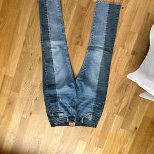 Tvåfärgade Jeans  - Säljer ett par unika tvåfärgade jeansbyxor från Driftwood (köpta på Bloomindales i USA) i blå och mörkgrå denim. Byxorna har normal passform, klassiska fem fickor och dragkedja. Snygg kontrast mellan färgblocken längs benen. Dem är raka i modellen och något cropped!