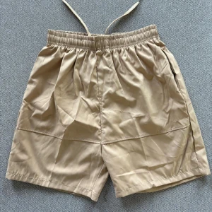Beiga shorts med snörning - Snygga beiga shorts med elastisk midja och snörning. De har en normal passform och är tillverkade i ett lätt och mjukt material, perfekta för varma dagar.
