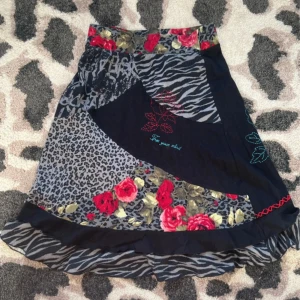 Kjol med djurmönster - Unik kjol från KappAhl i patchworkstil med leopard- och zebramönster samt röda rosor. Broderad röd blomma och texten 'Free your mind' framtill. Svart bas med volangkant nertill. Perfekt statementplagg för dig som gillar mönster och färg. Storlek 32/34, men sitter bra på mig som vanligtvis har S/M. Den är stretchig 