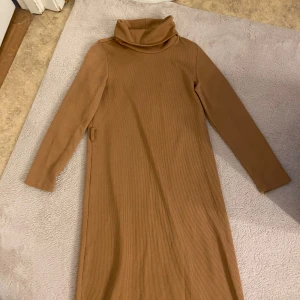 Beige ribbad långklänning med polokrage från Koton - Säljer en beige ribbad långklänning från Koton med lång ärm och hög polokrage. Tappat bort snöret.