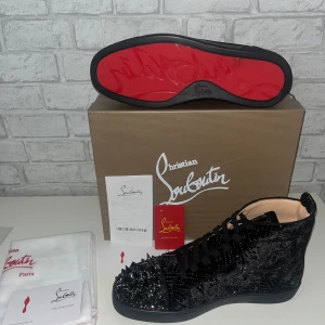 Svarta sneakers med nitar från Christian Louboutin - Säljer ett par svarta sneakers från Christian Louboutin med glittriga detaljer och svarta nitar på tån. Skorna har klassisk röd sula, snörning och lyxig känsla. Perfekta för dig som vill sticka ut med en exklusiv look. (19)