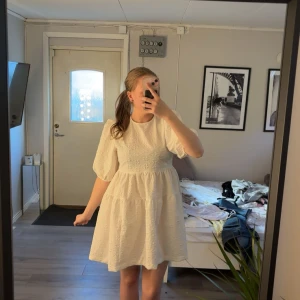 Vit kortklänning med puffärmar och knyt i ryggen - Så fin vit klänning med puffiga kortärmar och strukturmönster i tyget. Klänningen har rund halsringning och två knytband i ryggen som ger en öppen rygg-detalj. Perfekt för sommarens alla tillfällen och skolavslutning🤍🥰