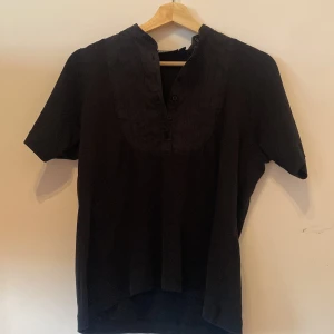 Svart kortärmad skjorta från Machine - Svart skjorta från Machine i storlek M. Skjortan har korta ärmar, knappar framtill och en markerad krage med diskreta sömmar. 