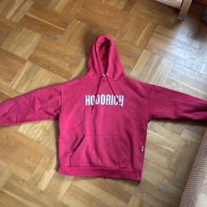 Röd hoodie från Hoodrich - Säljer en röd hoodie från Hoodrich med vit logga på bröstet. Tröjan har huva och stor magficka. Perfekt för dig som gillar streetwear och vill ha en skön och snygg tröja.