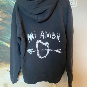 Mi amor hoodie - Svart hoodie från Mira Paris med vit text 'Mi Amor' och ett hjärta med pil på ryggen. Tröjan har huva, magficka och långa ärmar. Väll använd därav priset! Ny pris ≈1500