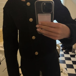 Svart cardigan jacka från Gina Tricot - Svart överdel med guldknappar från Gina Tricot. Går att använda som jacka och som tjockare tröja. I storlek S. I mycket bra skick. 