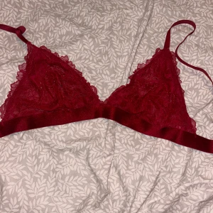 Röd spets bralette från H&M - Säljer en röd bralette i spets från H&M. Modellen är ärmlös med tunna axelband och dekorativa spetsdetaljer. .