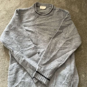 BlåGrå ulltröja från Lacoste - Skick:8/10 mycket bra. Obs lappen är solbränd så man ser inte riktigt! Pris: 399kr
