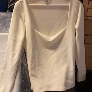 Vit långärmad topp med djup urringning - Säljer en stilren vit topp med lång ärm och djup urringning framtill. Perfekt för dig som gillar en enkel men snygg look. Passar till många olika outfits!