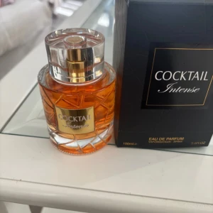 Cocktail Intense Eau de Parfum - Cocktail Intense Eau de Parfum i en elegant glasflaska med guldiga detaljer och ett diamantmönstrat mönster. Parfymen har en varm bärnstensfärgad vätska och kommer i en svart lyxig kartong med guldtext. Flaskan rymmer 100 ml.