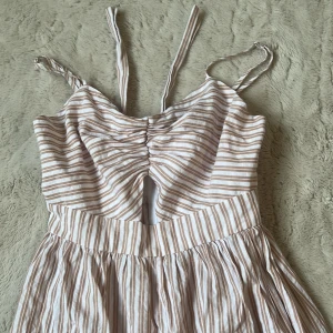 Beige och vit randig klänning från NA-KD - Superfin sommarklänning från NA-KD i beige och vitt med smala ränder. Axelbandslös look med knytband upptill och liten cut-out framtill. Köpt för 499kr💞