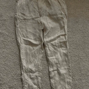 Beige linnebyxor från Zara - Säljer ett par ljusbeige linnebyxor från Zara med normal passform. Byxorna har knäppning fram, sidfickor och två bakfickor. Perfekta för varmare dagar och ger en avslappnad men stilren look.                                            Knappt använda
