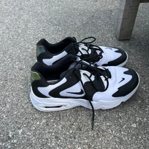 Nike sneakers i svart och vitt - Säljer ett par snygga Nike sneakers i svart och vitt med coola detaljer och svart snörning. Skorna har en sportig look och passar perfekt till vardags eller träning. Klassisk Nike-logga på sidan och bekväm platt sula.