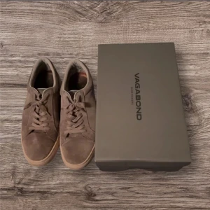 Bruna sneakers från Vagabond - Säljer ett par bruna sneakers från Vagabond i mocka med rund tå och platt sula. Skorna har snörning och en stilren design som passar till många olika outfits. Perfekta för dig som gillar klassiska och bekväma skor.