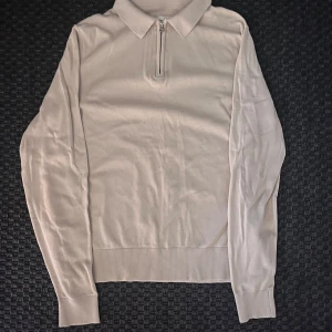 Beige långärmad tröja med dragkedja från These Glory Days - Säljer en stilren beige långärmad tröja från These Glory Days i mjuk bomull. Tröjan har krage och kort dragkedja framtill, perfekt för en clean och avslappnad look.