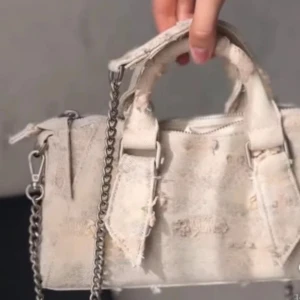 Vit axelväska i jeansmaterial med kedja - Säljer en vit/beige väska i jeansmaterial med slitna detaljer och silverfärgad kedja. Aldrig använd från Zara