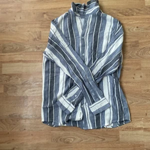 Randig linneskjorta från 157 - Säljer en snygg randig skjorta i blått och vitt från 157. Skjortan är i svalt linne, har långa ärmar och knäppning framtill. Perfekt för en avslappnad och stilren look.