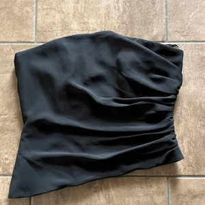 Svart korsett från Alfred Sung - Säljer en elegant svart korsett från Alfred Sung. Toppen är axelbandslös och har en figurnära passform. Perfekt för att skapa en stilren look. Storlek M, normal i storlek. Bredd=39cm, längd=35cm