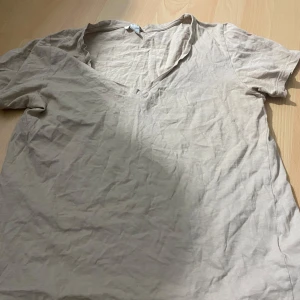 Beige v-ringad t-shirt från Amisu - Säljer en beige t-shirt från Amisu med v-ringning och korta ärmar. Perfekt basic-plagg som passar till det mesta. Tillverkad i mjukt material för en skön känsla.