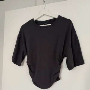 Grå t-shirt från Gina Tricot - En mörkgrå basic t-shirt från Gina Tricot med rund halsringning och avslappnad passform. T-shirten sitter åt vid midjan och har vida ärmar