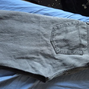 Grå Levi's 501 jeans straight fit - Säljer ett par klassiska grå Levi's 501 jeans med raka ben och normal passform. Jeansen har fem fickor, knappgylf och är tillverkade i 100% bomull. Perfekta för dig som gillar en tidlös och avslappnad look.