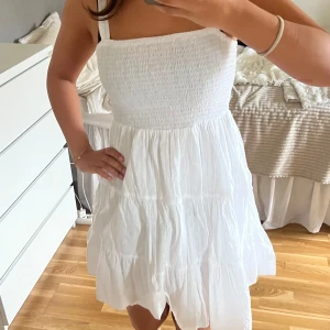 Vit somrig kortklänning från Primark - Supersöt vit kortklänning från Primark med smockad överdel och tunna axelband. Kjolen är volangig och luftig, perfekt för varma dagar. Klänningen har en enkel och fräsch look som passar till sneakers eller sandaler.