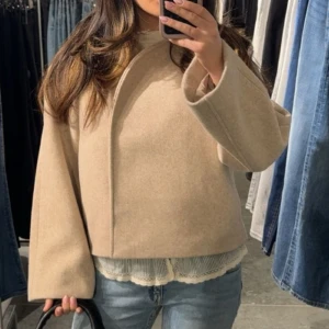 Beige kappa med vida ärmar - Snygg beige kappa med minimalistisk design och vida ärmar. Jackan har en boxig, loose passform och är tillverkad i ett mjukt ullmaterial. Perfekt för dig som gillar stilrena och trendiga plagg med en clean look. pris går att diskutera 