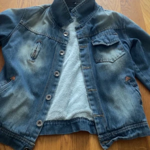 Metallica jeansjacka XL custom - Snygg jeansjacka i blå denim från Shi Phang Fu Shi, custommålad med Metallica Kill 'Em All-tryck på ryggen. Jackan har bruna spänndetaljer i midjan, bröstficka, knappar framtill och mjukt ljust foder. Perfekt för dig som vill sticka ut med en unik rockstil.