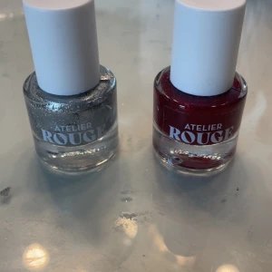 Atelier Rouge nagellack silver & röd - Två nagellack från Atelier Rouge, ett i glittrigt silver och ett i skimrande röd nyans. Båda kommer i rund glasflaska med vit kork. Perfekt för att skapa snygga naglar med extra glans och färg. Bara testade