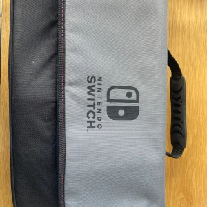 Nintendo Switch datorväska grå/svart - Säljer en snygg och praktisk datorväska från Nintendo Switch i grått och svart. Väskan har vadderat handtag, flera fack och smarta avdelare för konsol och tillbehör. Tillverkad i slitstark polyester med dragkedja och logga både utvändigt och invändigt. Och den är aldrig använd.