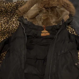 Svart dunjacka från Parajumpers S - Säljer en svart dunjacka från Parajumpers i storlek S funkar också som M. Jackan har en fluffig huva med fuskpäls, coolt gult spänne och dragkedja framtill. Perfekt för kalla dagar, har knappt använt den max bara 3 gånger den, är i väldigt bra skick köpte den ny men använder inte den längre.