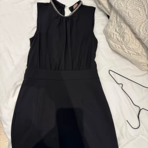 Svart ärmlös klänning med pärldetalj - Snygg svart ärmlös klänning med markerad midja och rund halsringning dekorerad med pärlor. Klänningen har en stilren och elegant look. Pris går att diskuteras!