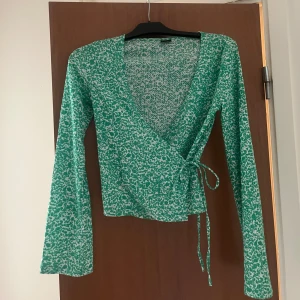 Grön omlottopp med knyt och mönster - Snygg grön omlottopp med vitt blommigt mönster och långa vida ärmar. Passar xs-m