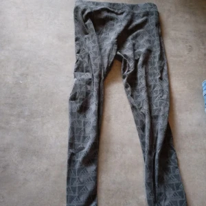 Grå Adidas leggings med logomönster - Snygga grå leggings från Adidas med all-over logomönster. Tight passform och stretchigt material som passar perfekt till träning eller chill. Klassisk Adidas-stil med diskret men ändå tydlig branding.