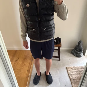Mörkblå  dunväst från Moncler (pris diskuteras) - Snygg mörkblå dunväst från Moncler med quiltad design och två dragkedjefickor framtill. Västen har en hög krage och klassisk Moncler-logga på bröstet. Perfekt att slänga över en hoodie eller tröja för en sportig vibe. Har kvitto, allt og medföljer. Köpt på NK 6999kr