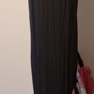 Svart långklänning med slits - Säljer en svart långklänning med hög hals och ärmlös design. Klänningen har en snygg slits på ena sidan