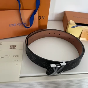 Louis Vuitton svart monogram bälte - Snyggt svart bälte från Louis Vuitton med klassiskt monogrammönster och stor LV-logga i silver på spännet. Bältet är gjort i exklusivt skinn och har en stilren, rak form. Perfekt för dig som vill ha en lyxig accessoar med ikonisk design. Kommer med box och kvitto m.m