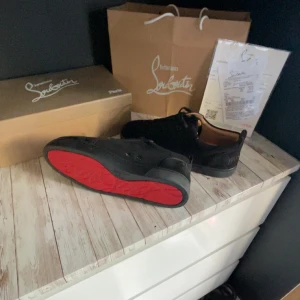 Svarta sneakers från Christian Louboutin - Snygga svarta sneakers från Christian Louboutin med ikonisk röd sula. Skorna har rund tå, snörning och är tillverkade i skinn och mocka. Perfekta för dig som vill sticka ut med exklusiva detaljer och klassisk design.
