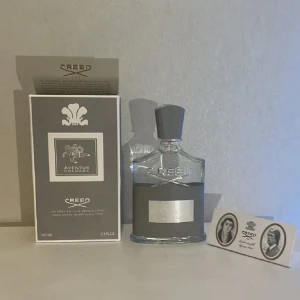 Creed Aventus Cologne 100ml - Lyxig parfym från Creed, Aventus Cologne, 100ml. Flaskan är transparent med grå etikett och silverdetaljer, samt en grå kork med silveremblem på toppen. Kommer med originalkartong och informationskort. En ikonisk och elegant doft för dig som gillar exklusiva parfymer.