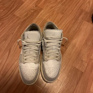 Jordan 1 Low SE craft  - Snygga Nike Air Jordan 1 Low sneakers i vitt och beige med klassisk Jordan-logga på hälen. Perfekta för dig som gillar streetwear och sneakers. De kommer rengöras vid köp